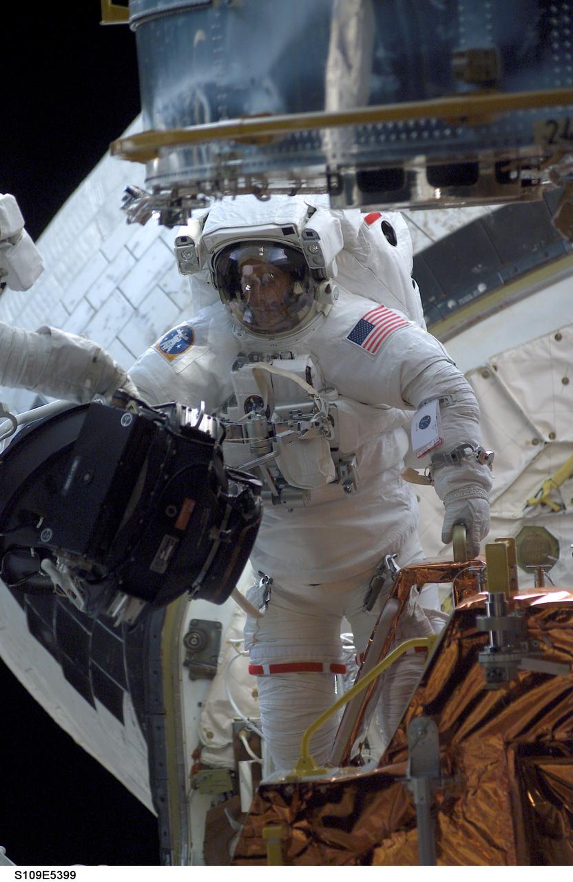 STS109-E-5399 (5 March 2002) --- Astronaut James H. Newman, mission specialist, moves about in the Space Shuttle Columbia's cargo bay while working in tandem with astronaut Michael J. Massimino (out of frame), mission specialist, during the STS-109 mission's second day of extravehicular activity (EVA).  Inside Columbia's cabin, astronaut Nancy J. Currie, mission specialist, controlled the Remote Manipulator System (RMS) to assist the two in their work on the Hubble Space Telescope (HST). Part of the giant telescope's base, latched down in the payload bay, can be seen just above Newman.  The image was recorded with a digital still camera.