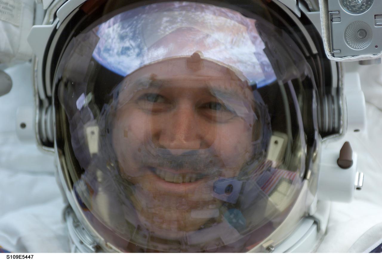 STS109-E-5447 (4 March 2002) --- Astronaut John M. Grunsfeld, payload commander, peers into the crew cabin of the Space Shuttle Columbia during the first STS-109 extravehicular activity (EVA-1) on March 4, 2002.  Grunsfeld's helmet visor displays a mirrored image of the Earth's hemisphere.  Astronauts Grunsfeld and Richard M. Linnehan replaced the starboard solar array on the Hubble Space Telescope (HST) on the first of five scheduled STS-109 space walks.  The image was recorded with a digital still camera by a crewmate on shuttle's aft flight deck.