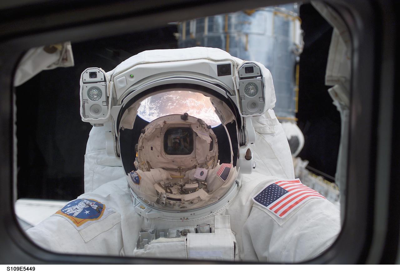STS109-E-5449 (4 March 2002) --- Astronaut John M. Grunsfeld, payload commander, peers into the crew cabin of the Space Shuttle Columbia during the first STS-109 extravehicular activity (EVA-1) on March 4, 2002. Grunsfeld's helmet visor, with the sunshield now in place, displays mirrored images of the Earth's hemisphere and the Space Shuttle Columbia's aft cabin. The distorted reflection gives the crew cabin a cyclops-like appearance. Astronauts Grunsfeld and Richard M. Linnehan replaced the starboard solar array on the Hubble Space Telescope (HST) on the first of five scheduled STS-109 space walks. The lower portion of the giant telescope can be seen behind the payload commander. The image was recorded with a digital still camera by a crewmate on shuttle's aft flight deck.