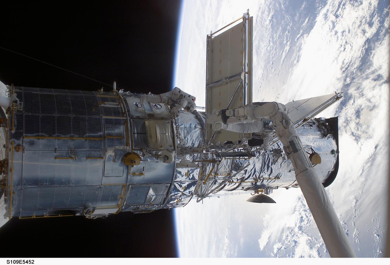 STS109-E-5452 (4 March 2002) --- Astronauts Richard M. Linnehan (partially visible on the end of Columbia's robotic arm), STS-109 mission specialist, and John M. Grunsfeld  (center frame), payload commander, work to replace the starboard solar array on the Hubble Space Telescope (HST). Linnehan works while anchored to a foot restraint connected to the shuttle's Remote Manipulator System (RMS), controlled inside the shuttle's crew cabin by astronaut Nancy J. Currie, mission specialist. The image was   recorded with a digital still camera.