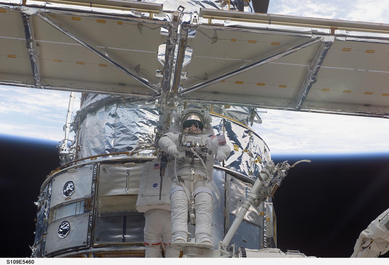 STS109-E-5460 (4 March 2002) --- Astronauts Richard M. Linnehan (facing camera, frame center), STS-109 mission specialist, and John M. Grunsfeld (partially obscured behind Linnehan), payload commander, work to replace the starboard solar array on the Hubble Space Telescope (HST). Linnehan is standing on a foot restraint connected to the Space Shuttle Columbia's Remote Manipulator System (RMS) robotic arm, controlled inside the shuttle's crew cabin by astronaut Nancy J. Currie, mission specialist. The image was recorded with a digital still camera.