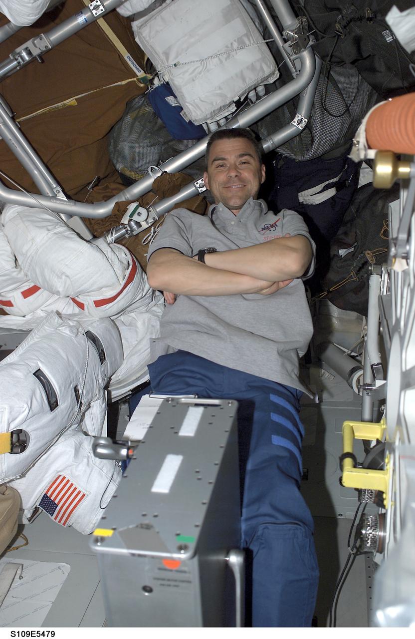 STS109-E-5479 (7 March 2002)-- Astronaut Duane G. Carey, STS-109 pilot, takes a leisurely &quot;spin&quot; on the bicycle ergometer on the mid deck of the Space Shuttle Columbia, while waiting to assist Flight Day 7's assigned space walkers--astronaut James H. Newman and Michael J. Massimino. The extravehicular mobility unit (EMU) space suits of the two can be seen in the background.  The image was recorded with a digital still camera.