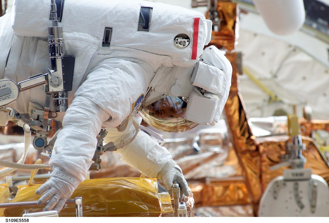 STS109-E-5558 (8 March 2002) --- Astronauts John M. Grunsfeld, payload commander, and Richard M. Linnehan (out of frame) mission specialist, participate in the final of five STS-109 space walks. The two went on to install an experimental cooling system for the Hubble Space Telescope’s infrared Camera and Multi-Object Spectrometer (NICMOS). This image was recorded with a digital still camera by a crewmate inside the shuttle's crew cabin. The NICMOS has been dormant since January 1999 when its original coolant ran out.