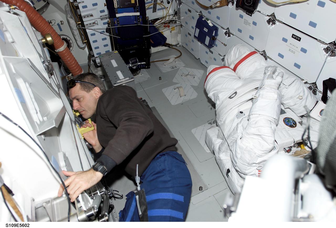 STS109-E-5602 (5 March 2002) --- Astronaut Richard M. Linnehan, mission specialist, checks the airlock hatch as two crewmates on the other side, equipped with extravehicular mobility units (EMU) space suits, start their extravehicular activity (EVA). On the previous day astronauts Linnehan and John M. Grunsfeld replaced the starboard solar array on the Hubble Space Telescope (HST). This day's space walk went on to see astronauts James H. Newman and Michael J. Massimino replace the port solar array. Grunsfeld's suit, scheduled for two more space walks, is temporarily stowed on the mid deck floor at right. The image was recorded with a digital still camera.