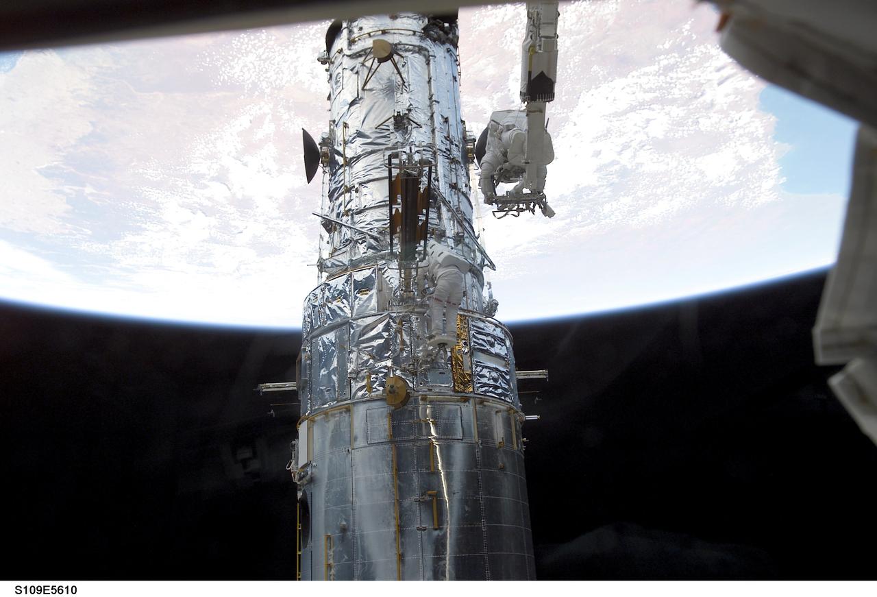 STS109-E-5610 (5 March 2002) --- Astronauts James H. Newman, attached to the Remote Manipulator System (RMS) arm of the Space Shuttle Columbia, and Michael J. Massimino (barely visible against the Hubble Space Telescope near center frame) work on the telescope as the shuttle flies over Australia. This day's space walk went on to see astronauts Newman and Massimino replace the port solar array on the Hubble. On the previous day astronauts John M. Grunsfeld and Richard M. Linnehan replaced the starboard solar array on the giant telescope. The image was recorded with a digital still camera.