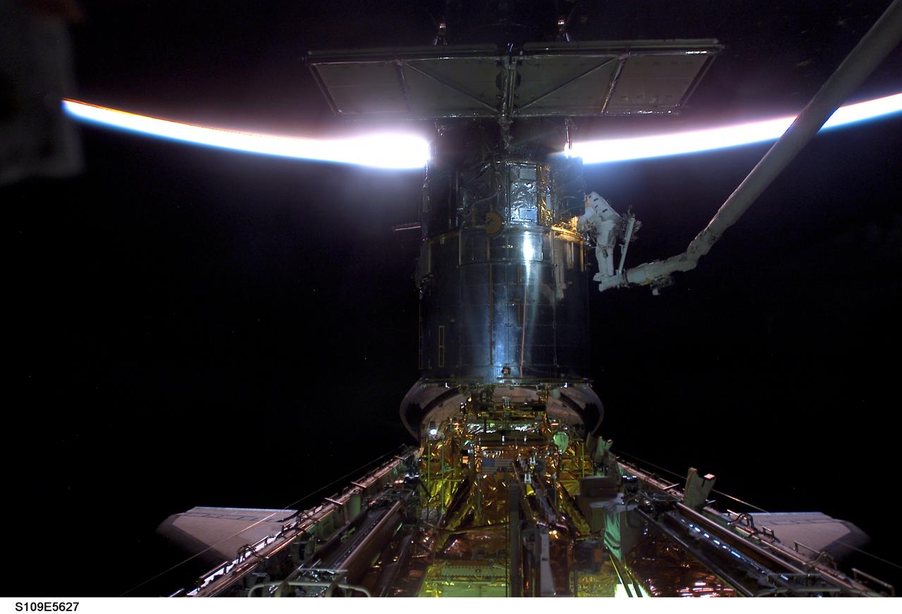 STS109-E-5627 (5 March 2002) --- With the Space Shuttle Columbia in limited natural light, two astronauts work on the Hubble Space Telescope (HST) during the flight's second of five scheduled space walks. A thin slice of reflected sunlight and airglow can be seen at Earth's horizon. Astronauts James H. Newman and Michael J. Massimino, mission specialists, are making their first extravehicular activity (EVA) of the mission, following the act of two other crewmembers on the previous day. Massimino can be identified on the end of the arm by the diagonal stripes on the pant legs of his extravehicular mobility unit (EMU) space suit. The image was recorded with a digital still camera.
