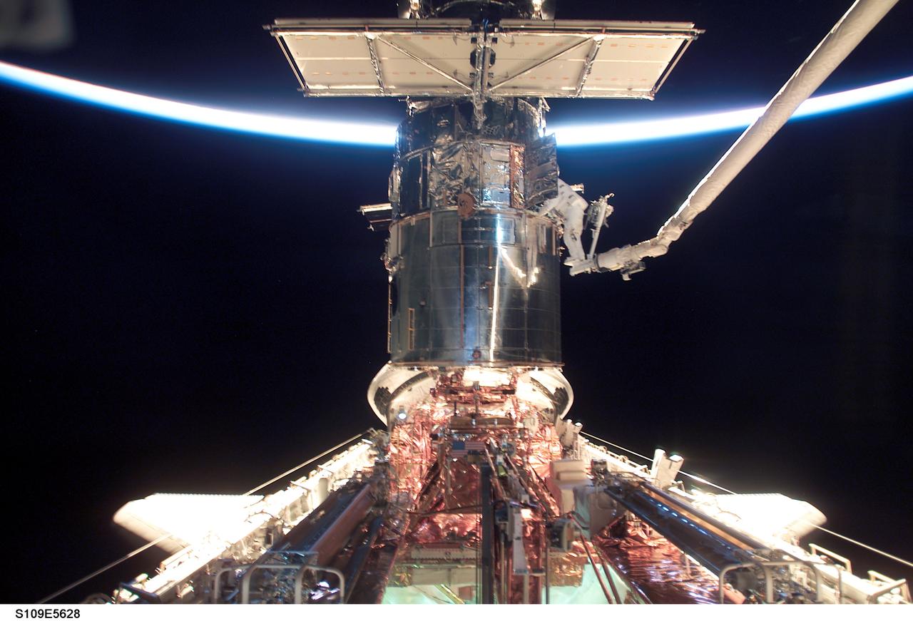 STS109-E-5628 (5 March 2002) --- With the Space Shuttle Columbia in limited natural light, two astronauts work on the Hubble Space Telescope (HST) during the flight's second of five scheduled space walks. A thin slice of reflected sunlight and airglow can be seen at Earth's horizon. Astronauts James H. Newman (out of frame) and Michael J. Massimino (on platform on end of robotic arm), mission specialists, are making their first extravehicular activity (EVA) of the mission, following the act of two other crewmembers on the previous day.  The image was recorded with a digital still camera.