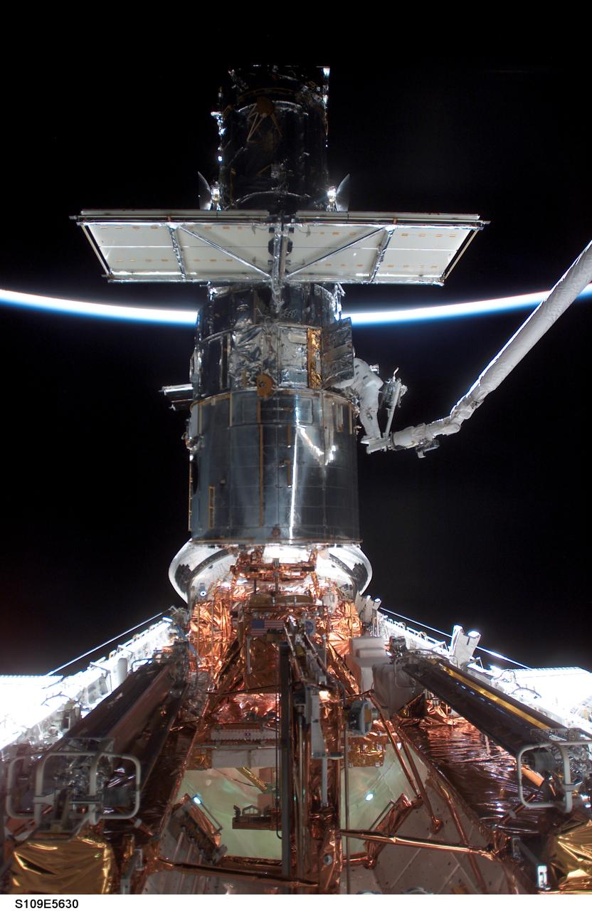 STS109-E-5630 (5 March 2002) --- With the Space Shuttle Columbia in limited natural light, two astronauts work on the Hubble Space Telescope (HST) during the flight's second of five scheduled space walks. A thin slice of reflected sunlight and airglow can be seen at Earth's horizon. Astronauts James H. Newman (out of frame) and Michael J. Massimino (on platform on end of robotic arm), mission specialists, are making their first extravehicular activity (EVA) of the mission, following the act of two other crewmembers on the previous day.  The image was recorded with a digital still camera.