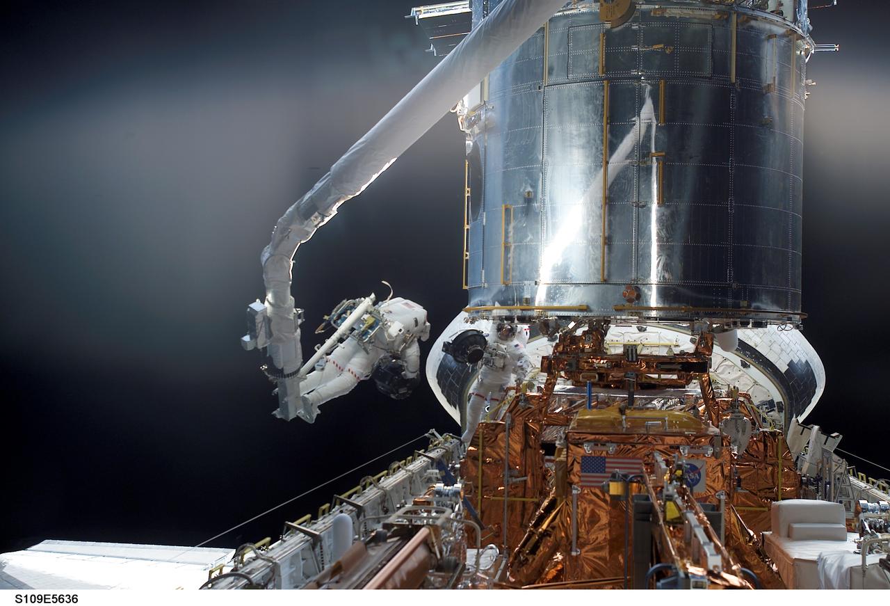 STS109-E-5636 (5 March 2002) --- Astronauts Michael J. Massimino (on the end of Columbia's robotic arm) and James H. Newman (positioned just to the right of Massimino above the shuttle's longerons) perform the second of five scheduled STS-109 space walks to service and upgrade the Hubble Space Telescope (HST). The image was recorded with a digital still camera.