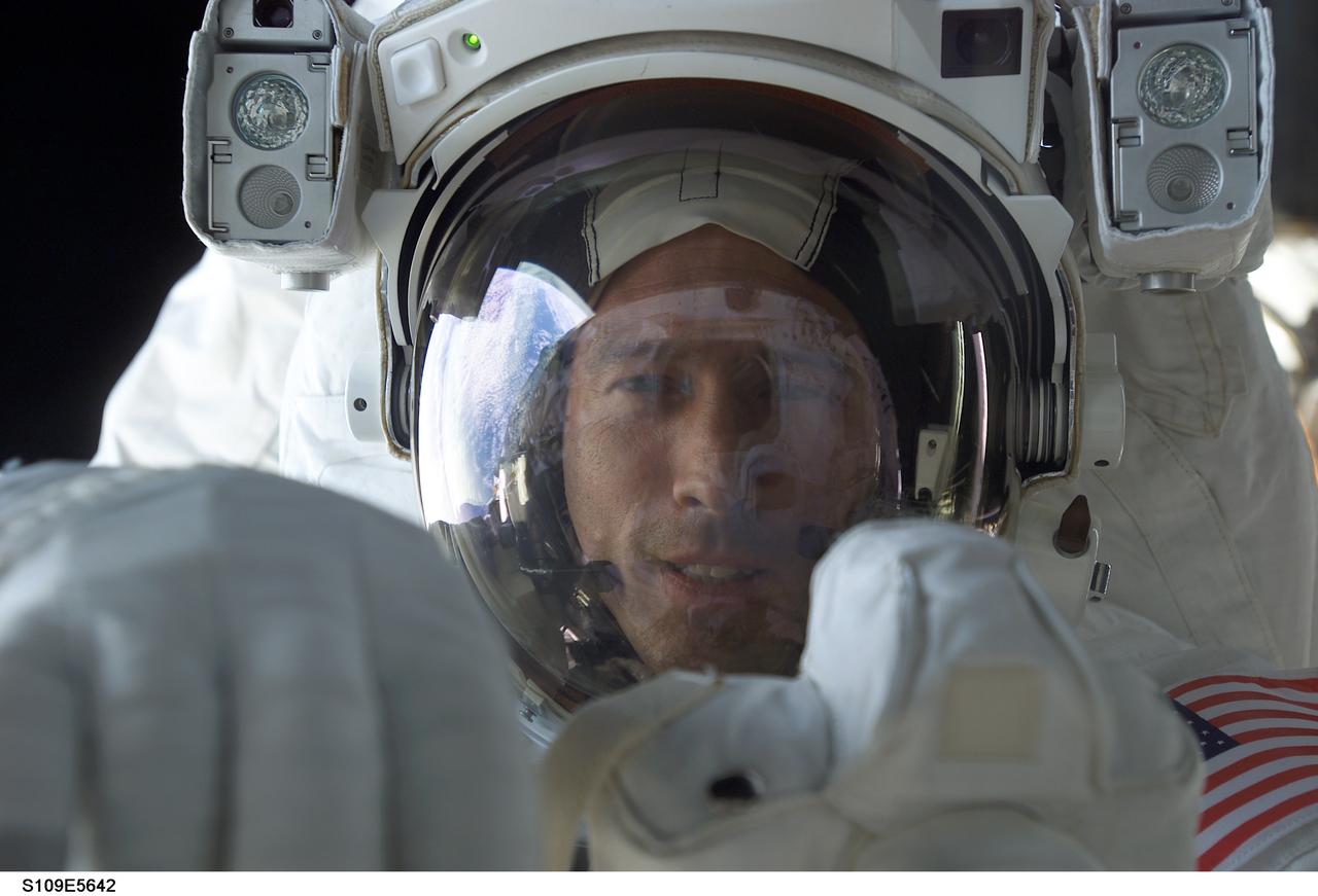 STS109-E-5642 (5 March 2002) ---  Astronaut James H. Newman, mission specialist, peers into Columbia's crew cabin during a brief break in work on the Hubble Space Telescope (HST), latched down just a few feet behind him in Columbia's cargo bay.  Astronauts Newman and Michael J. Massimino are making their first extravehicular activity (EVA) of the mission, following the act of two other crewmembers on the previous day.  The image was recorded with a digital still camera.