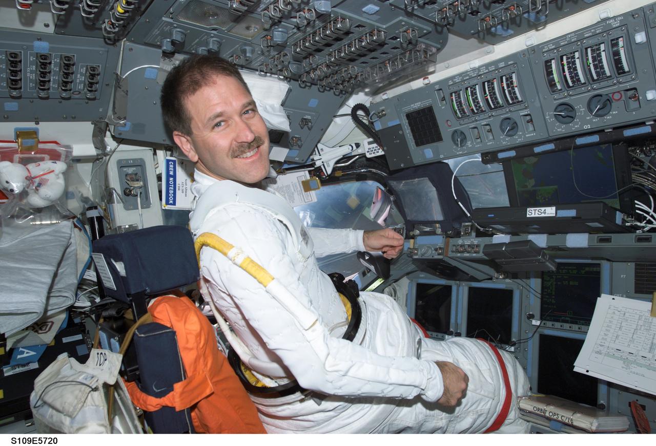 STS109-E-5720 (8 March 2002) --- Astronaut John M. Grunsfeld, STS-109 payload commander, wearing a portion of the extravehicular mobility unit (EMU) space suit, occupies the commander’s station on the forward flight deck of the Space Shuttle Columbia. The image was recorded with a digital still camera.