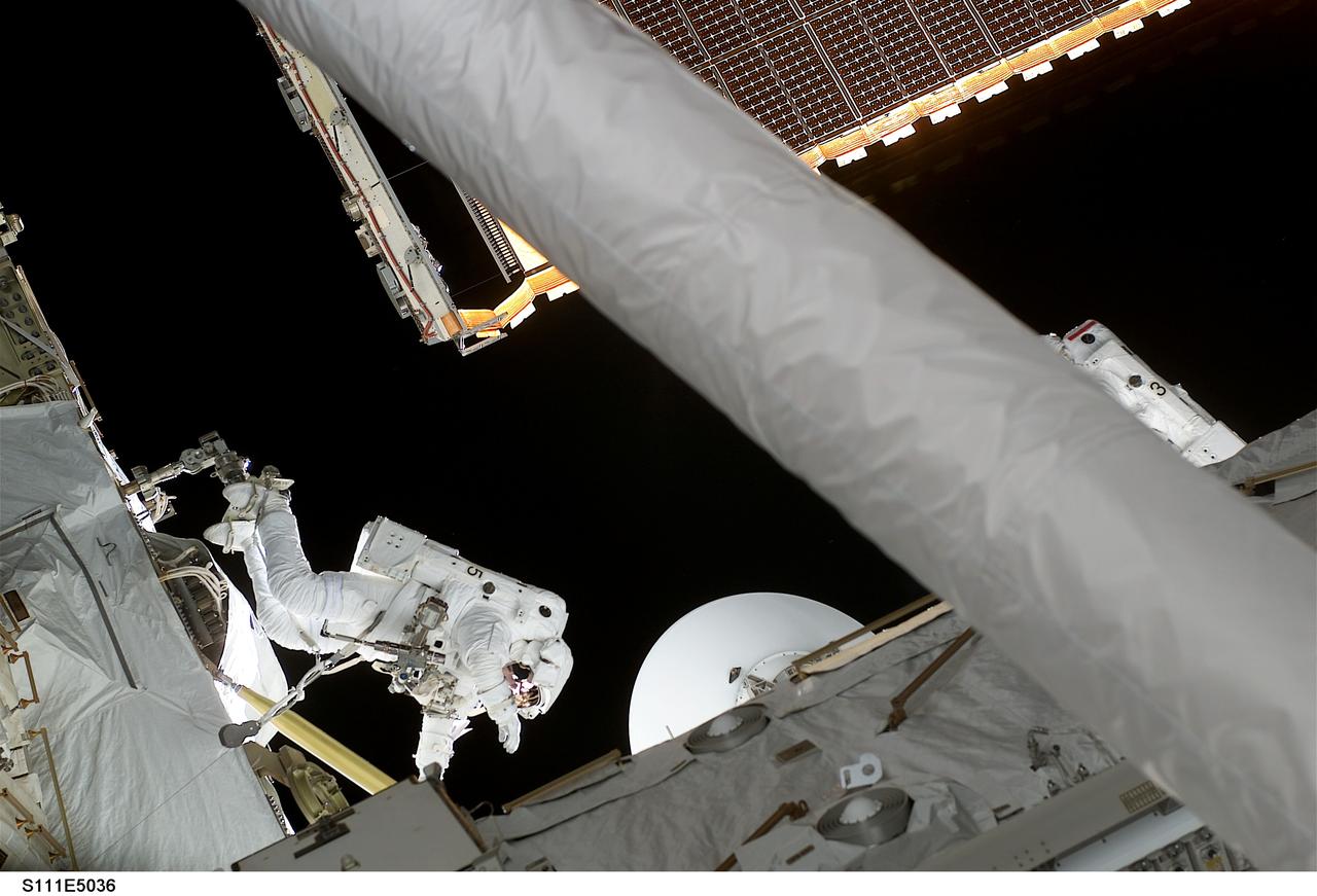 STS111-E-5036 (8 June 2002) --- Astronauts Philippe Perrin (left center) and Franklin R. Chang-Diaz (partially obscured by robot arm) work in chorus during extravehicular activity (EVA) to perform work on the International Space Station (ISS).  The first spacewalk of the STS-111 mission  began with the installation of a Power and Data Grapple Fixture (PDGF) for the station's robotic arm, known as Canadarm2, on the complex's P6 truss. The PDGF will allow the robotic arm to grip the P6 truss for future station assembly operations. Astronauts Chang-Diaz and  Perrin (with French Space Agency, CNES) went on to install the new fixture about halfway  up the P6 truss, the vertical structure that currently supports the station's set of large U.S. solar arrays.