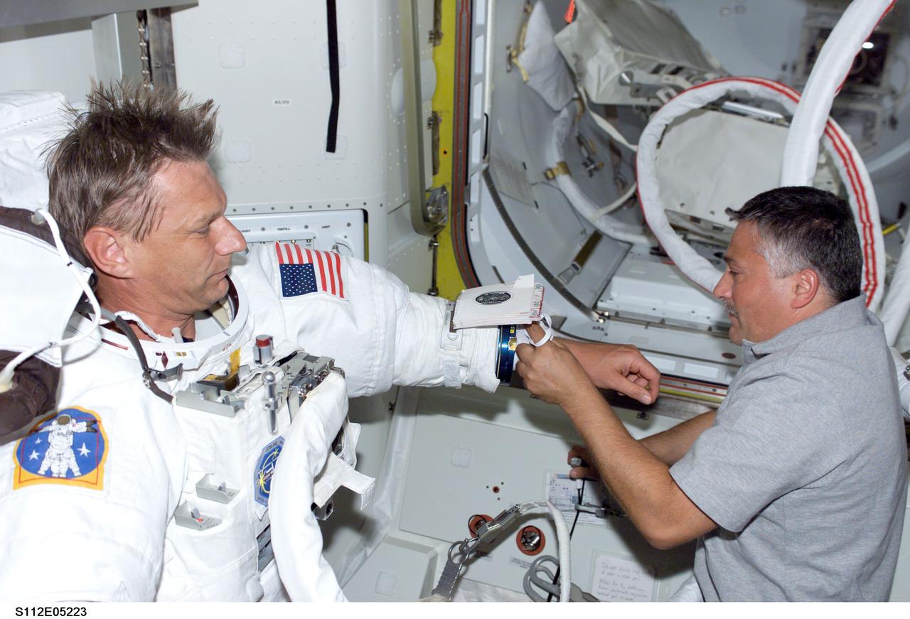 STS112-E-5223 (12 October 2002) --- Cosmonaut Fyodor Yurchikhin of Rosaviakosmos, STS-112 mission specialist, puts final touches on the extravehicular mobility unit (EMU) spacesuit of astronaut Piers J. Sellers prior to the mission's second spacewalk.