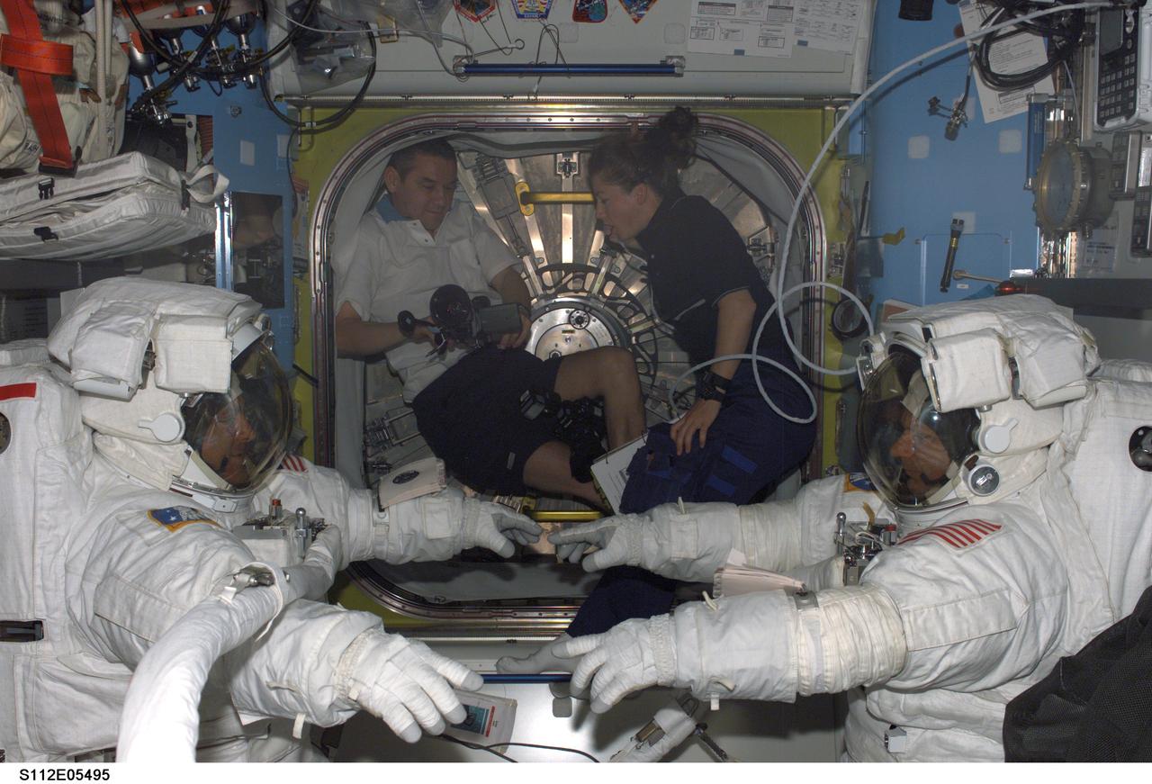 STS112-E-05495 (14 October 2002) --- Astronauts David A. Wolf (left) and Piers J. Sellers, STS-112 mission specialists attired in their Extravehicular Mobility Unit (EMU) space suits, are photographed in the Quest Airlock on the International Space Station (ISS) prior to the third scheduled session of extravehicular activity (EVA). Cosmonaut Valery G. Korzun (left), Expedition Five mission commander, and astronaut Pamela A. Melroy, STS-112 pilot, were visible in the background. Korzun represents Rosaviakosmos.