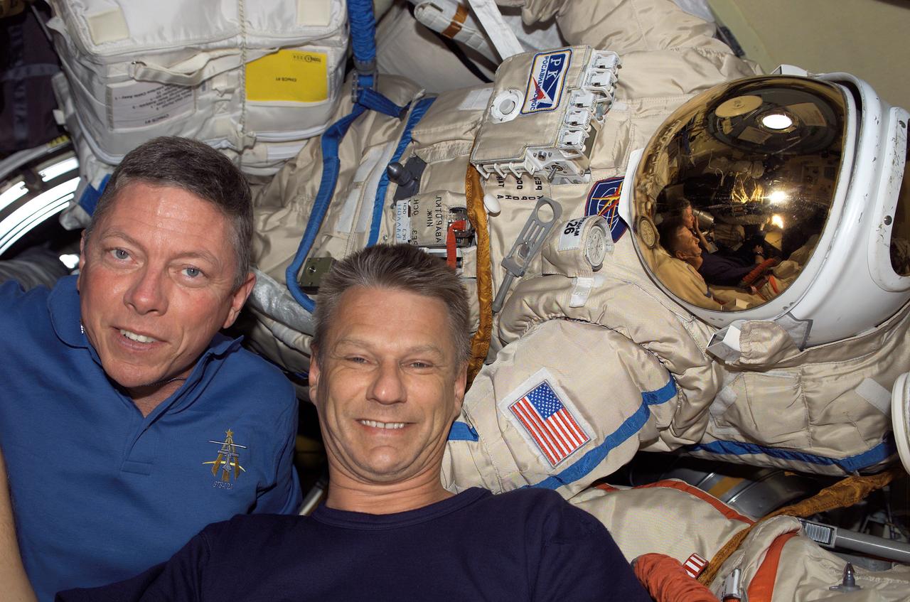 S121-E-06552 (13 July 2006) --- Astronauts Michael E. Fossum (left) and Piers J. Sellers, both STS-121 mission specialists, pose for a photo near a Russian Orlan space suit in the Pirs Docking Compartment of the International Space Station while Space Shuttle Discovery was docked with the station.