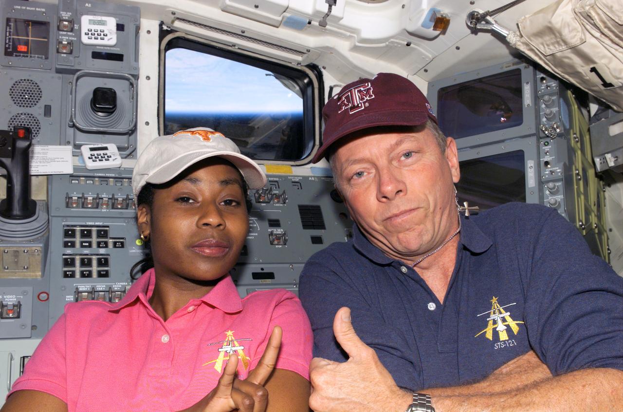 S121-E-08024 (16 July 2006) --- Astronauts Stephanie D. Wilson and Michael E. Fossum, STS-121 mission specialists, pose for a photo on the aft flight deck of the Space Shuttle Discovery. Fossum, a graduate of Texas A&M University, flashes the traditional "Gig 'Em, Aggies!" sign and wears an A&M cap, while UT alumnus Wilson gives the "Hook 'Em, Horns!" sign and wears the Longhorn cap. The two joked about the long-standing rivalry of their respective alma maters and have expressed looking forward to the Nov. 24 matchup between the two Big Twelve powers.