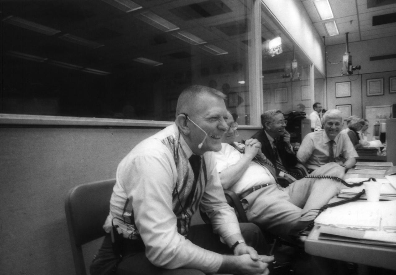 JSC officials, laughing, listen to crewmembers' commentary onboard Discovery, Orbiter Vehicle (OV) 103, during STS-26. In the Flight Control Room (FCR) of JSC's Mission Control Center (MCC) Bldg 30 and seated at the Mission Operations Directorate (MOD) console, MOD Director Eugene F. Kranz (foreground), wearing red, white and blue vest, smiles along with JSC Director Aaron Cohen and Flight Crew Operations Deputy Director Henry W. Hartsfield, Jr. (far right).
