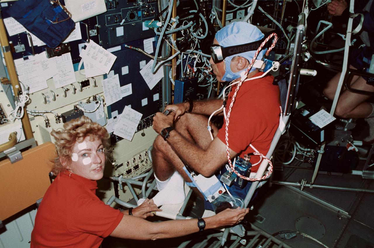 STS040-211-020 (5-14 June 1991) --- Vestibular experiment activities were captured onboard Columbia's Spacelab Life Sciences (SLS-1) module in this 35mm scene. Astronaut James P. Bagian, STS-40 mission specialist, is in a rotating chair while wearing an accelometer and electrodes to record head motion and horizontal and vertical eye movements during the rotations.  Payload specialist Millie Hughes-Fulford, lower left, assists with the test.