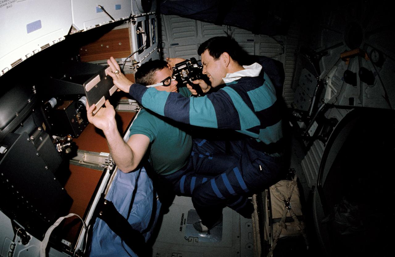 STS041-02-015 (6-10 Oct. 1990) --- A 35mm scene showing astronauts Robert D. Cabana (right), STS-41 pilot, and Bruce E. Melnick, mission specialist, participating in a detailed supplemental objective for STS-41 involving retinal photography. The hypothesis of this experiment is that retinal photographs taken on orbit will show evidence of increased intracranial pressure (ICP) and the evidence of increased ICP and the development of Space Adaptation Syndrome (SAS) will be correlated. SAS has been a subject of on-orbit analysis since the early days of space shuttle.