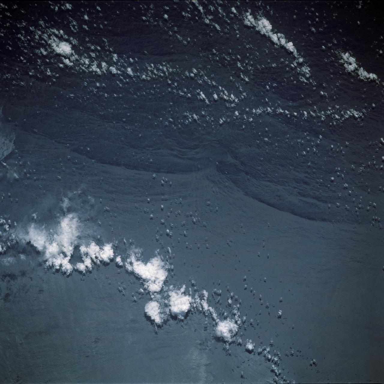 STS044-79-077 (24 Nov.-1 Dec. 1991) --- This photograph, captured from the Earth-orbiting Space Shuttle Atlantis, shows sunglint pattern in the western tropical Indian Ocean. Several large internal waves reflect around a shallow area on the sea floor. NASA scientists studying the STS-44 photography believe the shallow area to be a sediment (a submerged mountain) on top of the Mascarene Plateau, located northeast of Madagascar at approximately 5.6 degrees south latitude and 55.7 degrees east longitude. Internal waves are similar to surface ocean waves, except that they travel inside the water column along the boundary between water layers of different density. At the surface, their passage is marked on the sea surface by bands of smooth and rough water. These bands appear in the sunglint pattern as areas of brighter or darker water. NASA scientists point out that, when the waves encounter an obstacle, such as a near-surface seamount, they bend or refract around the obstacle in the same manner as surface waves bend around an island or headland.