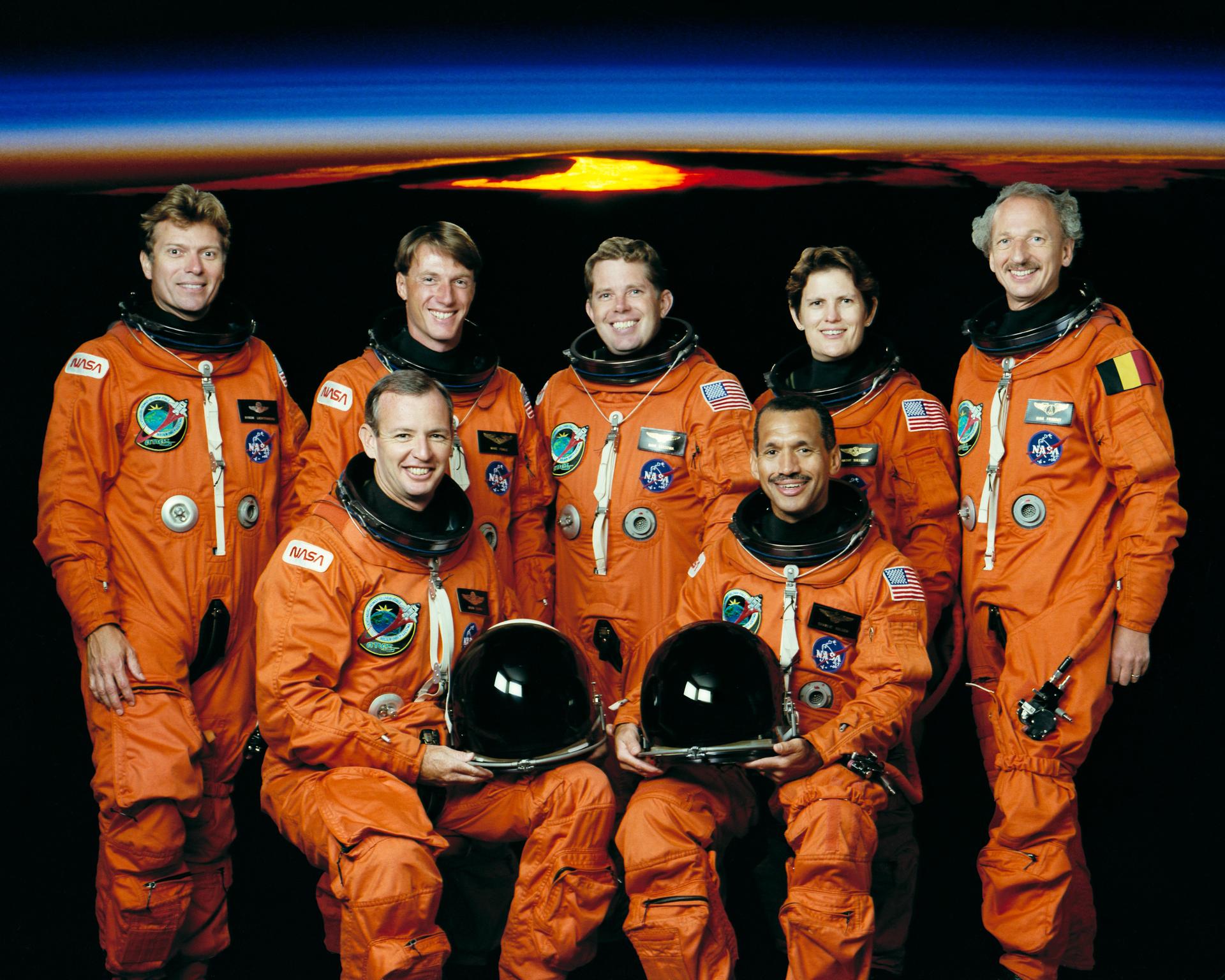 Seven astronauts in orange spacesuits pose for crew photo.