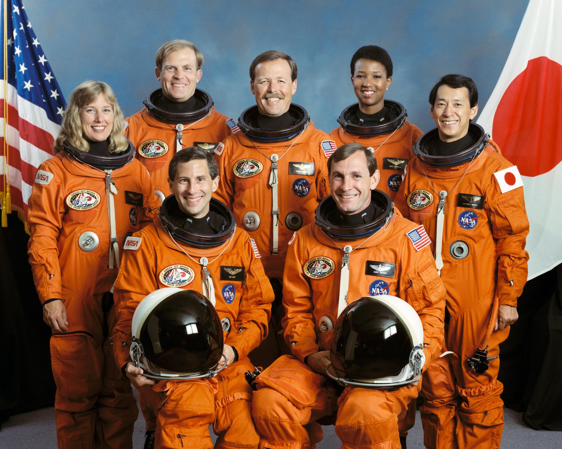 Astronauts - five men and two women, pose in front of an American flag and Japanese flag for crew photo.