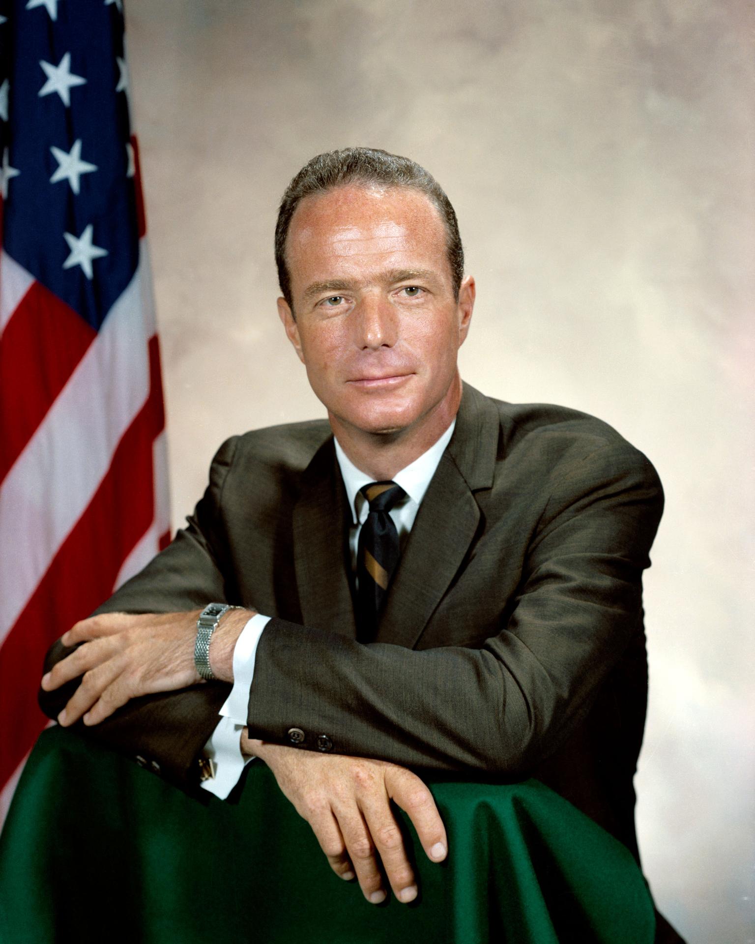 A man sits in front of the American flag and smiles