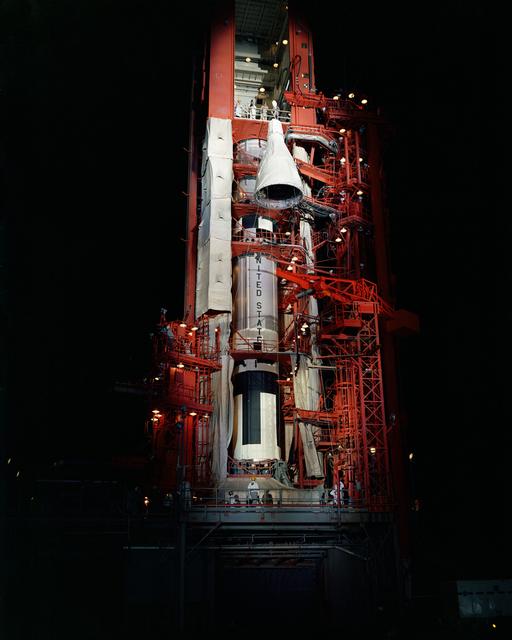 Nighttime scene of Gemini spacecraft being hoisted to top of Pad 19