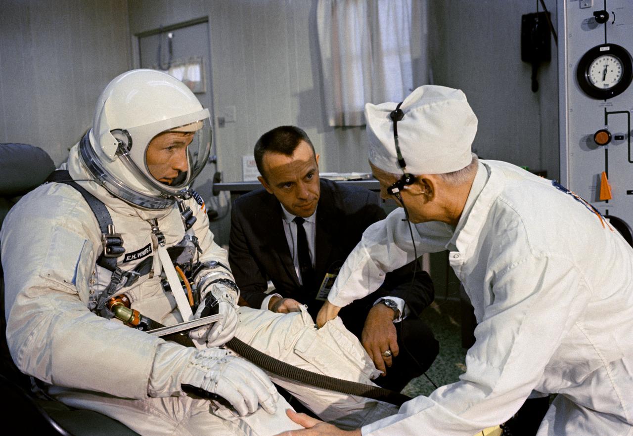 S65-29646 (3 June 1965) --- Astronaut Edward H. White II (left), Gemini-4 pilot, gets help with the donning of his spacesuit from a suit technician before the Gemini-4 spaceflight. Astronaut Alan Shepard is at center. The NASA Headquarter alternative photo number is 65-H-295.