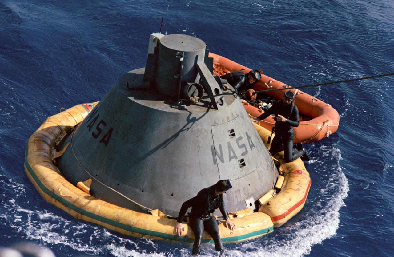 Apollo command module boilerplate floats in the Atlantic Ocean during a practice recovery exercise. Frogmen in a liferaft and on the flotation collar secure the command module boilerplate for hoisting onto a nearby recovery ship. The exercise was conducted in preparation for the forthcoming Apollo-Saturn 201 (AS-201) mission.