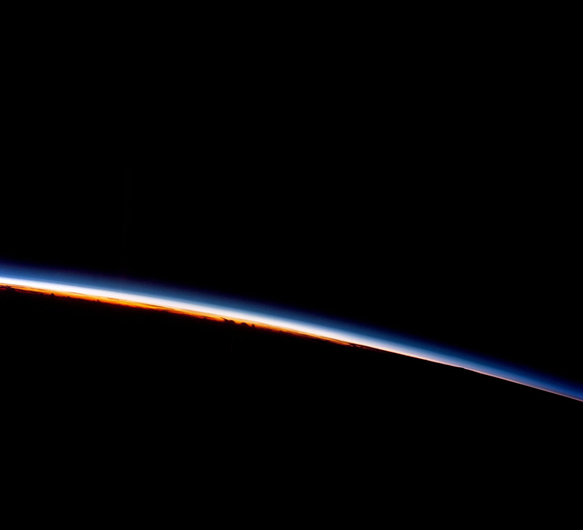 A sliver of Earth's atmosphere glows in bright colors as the sun rises over Guam, as seen by the astronauts of the Gemini 8 mission.