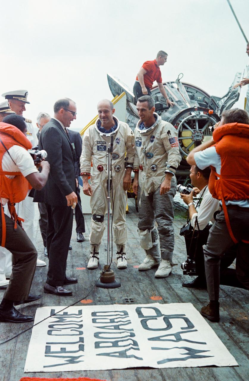 S66-34109 (6 June 1966) --- Astronauts Thomas Stafford and Eugene Cernan (right) receive a warm welcome as they arrive aboard the prime recovery ship, the aircraft carrier USS Wasp.  John C. Stonesifer, with the Manned Spacecraft Center's Landing and Recovery Division, stands next to microphone at left. The Gemini-9 spacecraft can be seen in the right background of the view. Photo credit: NASA