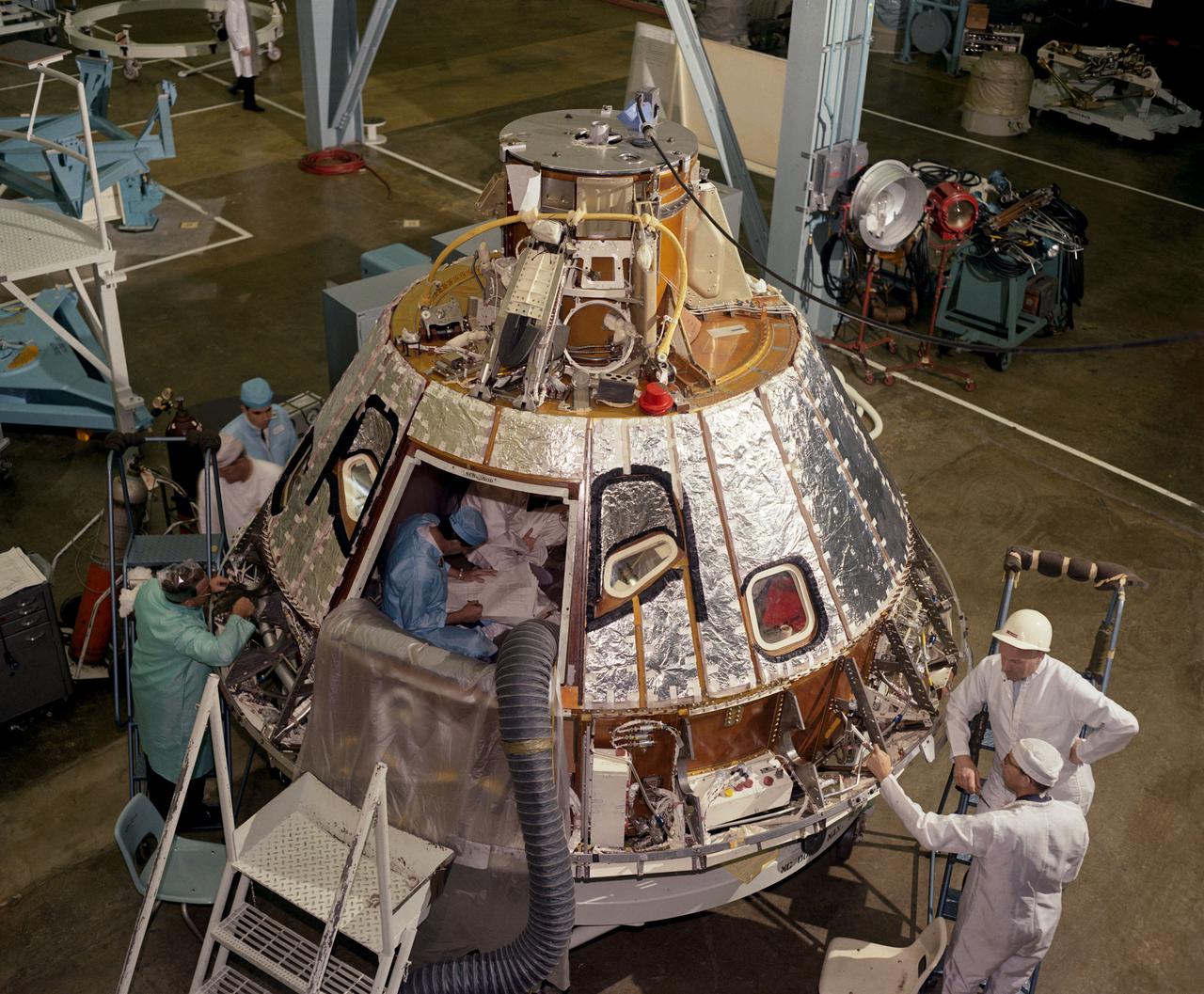 S66-41851 (1966) --- High angle view of Spacecraft 012 Command Module, looking toward -Z axis, during preparation for installation of the crew compartment heat shield, showing mechanics working on aft bay.