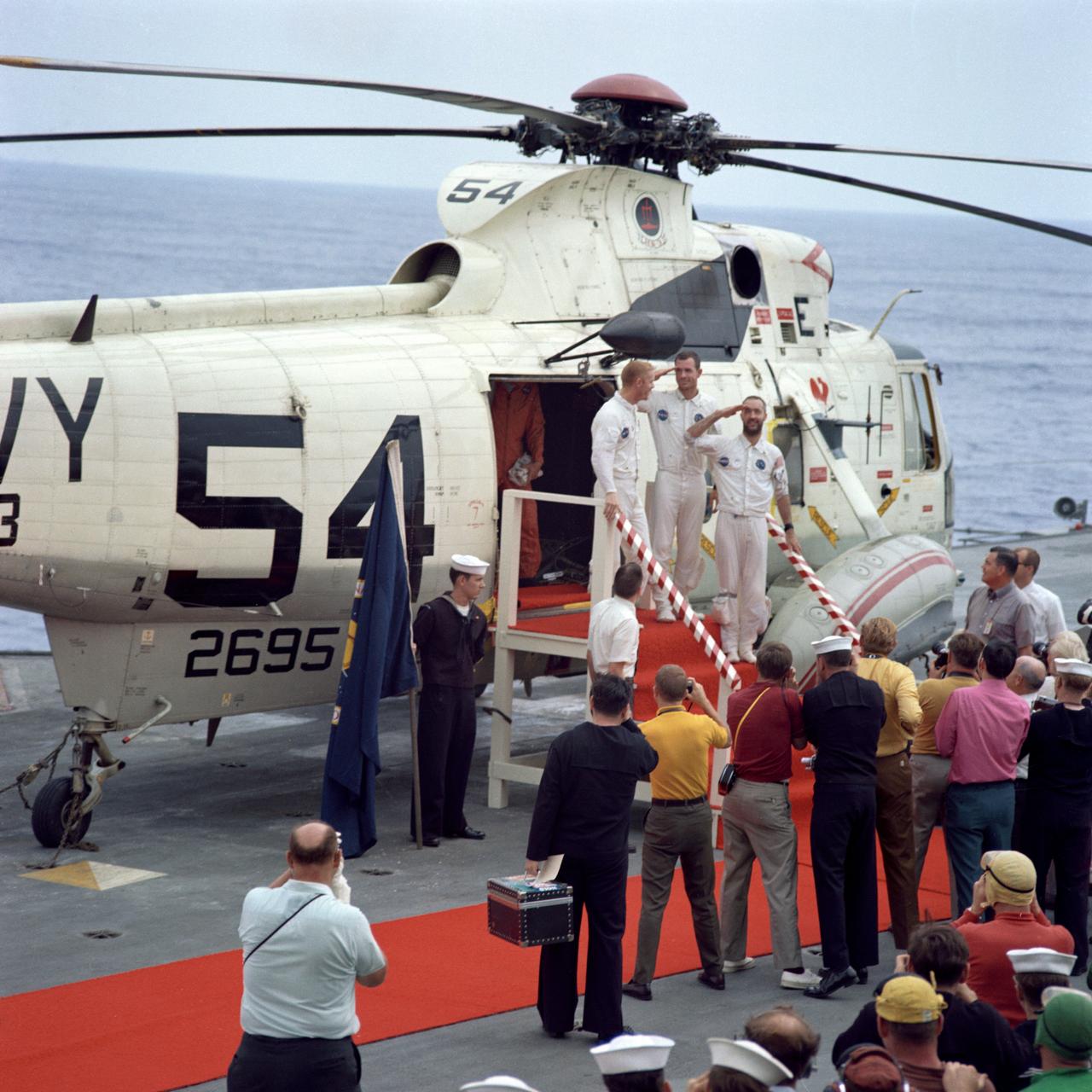 S69-20060 (13 March 1969) --- The Apollo 9 crewmen arrive aboard the USS Guadalcanal as they step from a helicopter to receive a red-carpet welcome. Two of the crewmen salute the crowd of newsmen, Navy and NASA personnel gathered to greet them. Left to right, are astronauts Russell L. Schweickart, lunar module pilot; David R. Scott (in back), command module pilot; and James A. McDivitt, commander. Splashdown occurred at 12:00:53 p.m. (EST), March 13, 1969, only 4.5 nautical miles from the USS Guadalcanal, prime recovery ship, to conclude a successful 10-day Earth-orbital space mission.