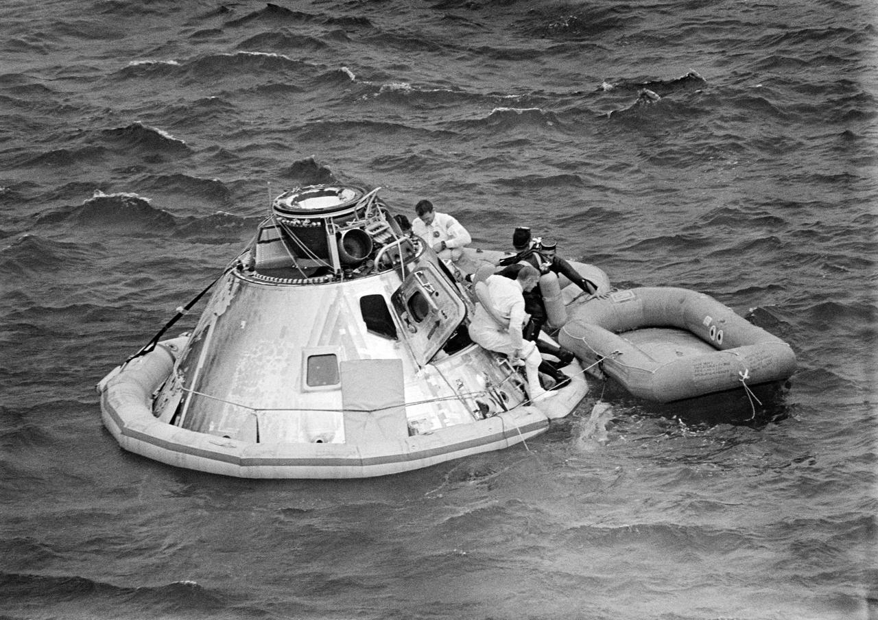 S69-27468 (13 March 1969) --- U.S. Navy underwater demolition team swimmers assist the Apollo 9 crew during recovery operations just after splashdown. They have already attached a flotation collar to the Command Module (CM). Astronaut Russell L. Schweickart, lunar module pilot, is about to climb into raft. In background is astronaut David R. Scott, command module pilot. Still inside the spacecraft is astronaut James A. McDivitt, commander. Splashdown occurred at 12:00:53 p.m. (EST), March 13, 1969, only 4.5 nautical miles from the prime recovery ship, USS Guadalcanal, to conclude a successful 10-day Earth-orbital mission in space.