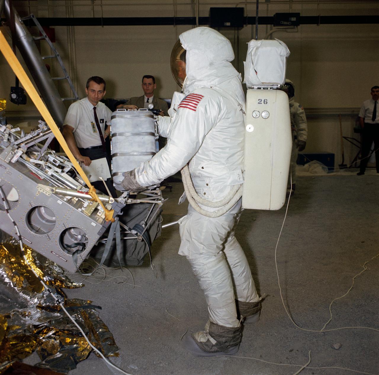 S69-31075 (18 April 1969) --- Suited astronaut Neil A. Armstrong, wearing an Extravehicular Mobility Unit (EMU), participates in lunar surface simulation training on April 18, 1969 in building 9, Manned Spacecraft Center (MSC).  Armstrong is prime crew commander of the Apollo 11 lunar landing mission.  Here, he is opening a sample return container.  On the right is the Modular Equipment Stowage Assembly (MESA) and the Lunar Module (LM) mockup.