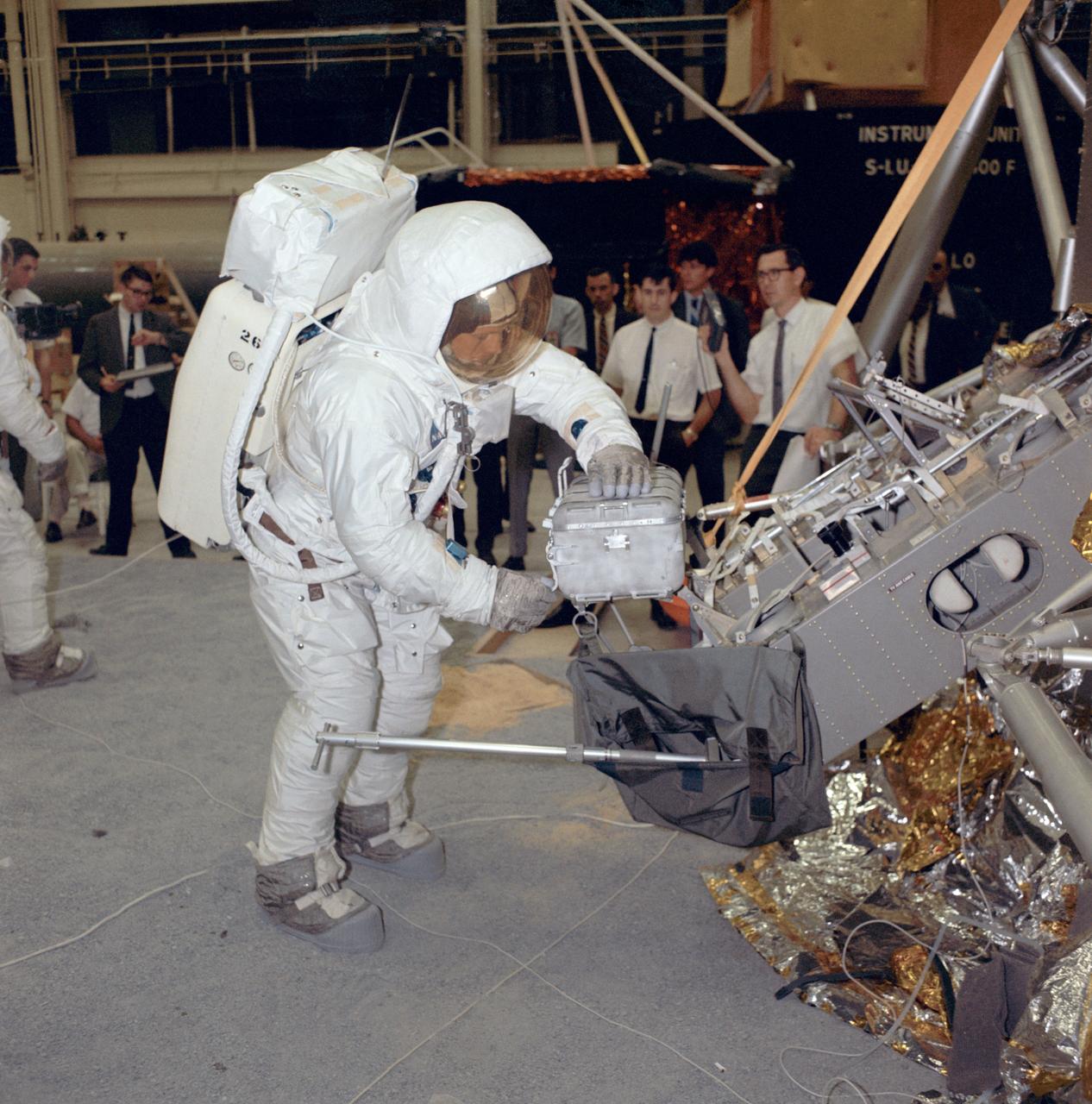 S69-31080 (18 April 1969) --- Suited astronaut Neil A. Armstrong, wearing an Extravehicular Mobility Unit (EMU), participates in lunar surface simulation training on April 18, 1969 in building 9, Manned Spacecraft Center (MSC). Armstrong is prime crew commander of the Apollo 11 lunar landing mission. Here, he is opening a sample return container. On the right is the Modular Equipment Stowage Assembly (MESA) and the Lunar Module (LM) mock-up.