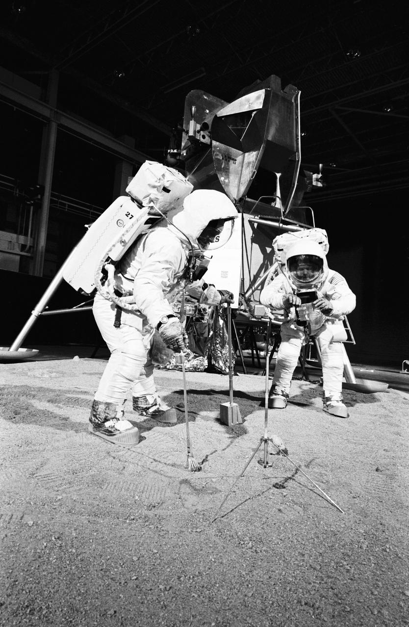 S69-32233 (22 April 1969) --- Two members of the Apollo 11 lunar landing mission participate in a simulation of deploying and using lunar tools on the surface of the moon.  The rehearsal took place during a training exercise in building 9 on April 22, 1969.  Astronaut Edwin E. Aldrin Jr. (on left), lunar module pilot, uses a scoop and tongs to pick up samples. Astronaut Neil A. Armstrong, Apollo 11 commander, holds the bag to receive the sample. In the background is a Lunar Module (LM) mock-up.