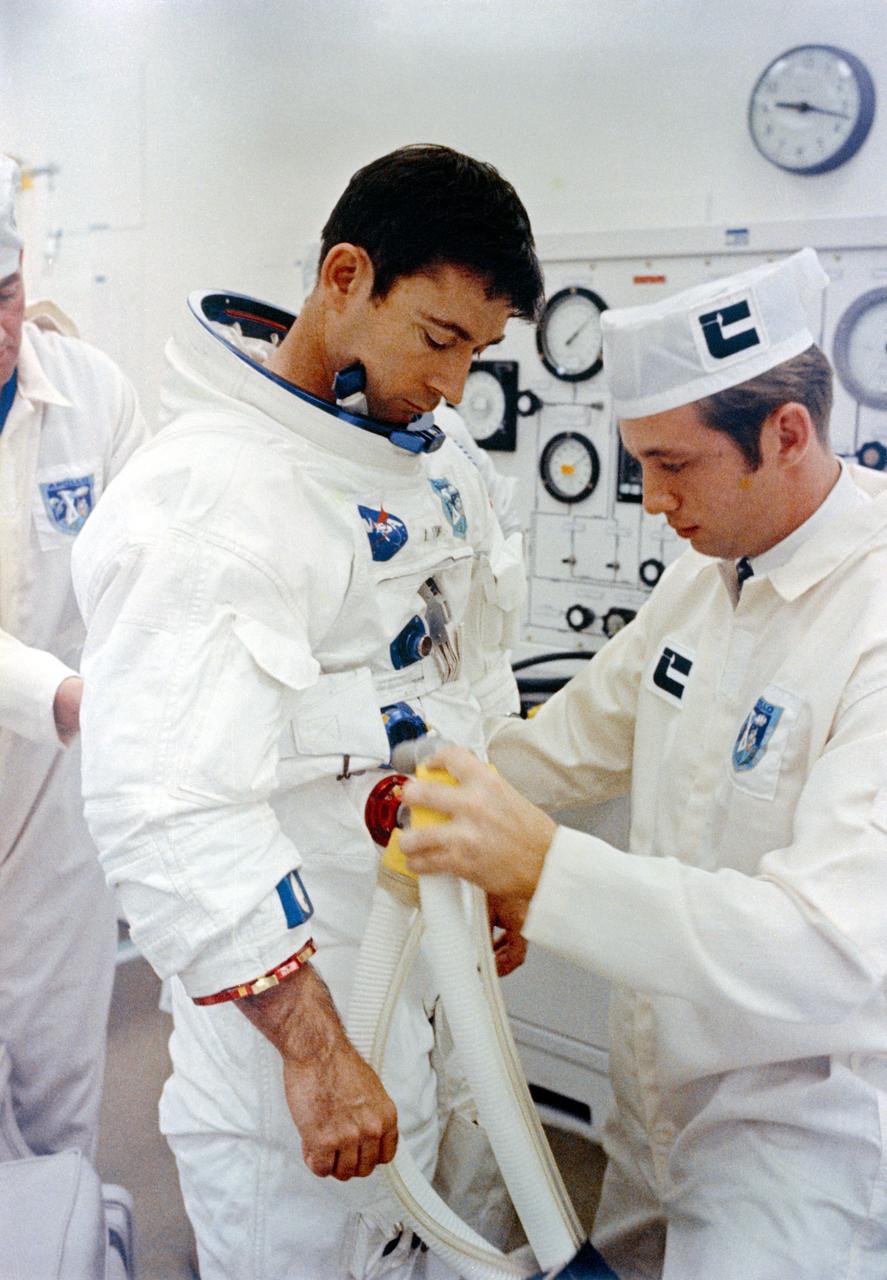 S69-34483 (18 May 1969) --- A technician attaches hose from test stand to spacesuit of astronaut John W. Young, Apollo 10 command module pilot, during final suiting operations for the Apollo 10 lunar orbit mission. Another technician makes adjustment behind Young. Minutes later astronauts Young; Thomas P. Stafford, commander; and Eugene A. Cernan, lunar module pilot, rode a transfer van from the Kennedy Space Center's Manned Spacecraft Operations Building over to Pad B, Launch Complex 39, where their spacecraft awaited them. Liftoff was at 12:49 p.m. (EDT), May 18, 1969.