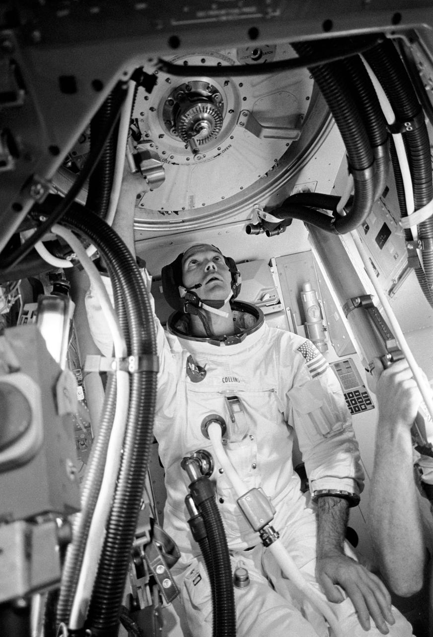 S69-38323 (28 June 1969) --- Astronaut Michael Collins, command module pilot of the Apollo 11 flight, is seen inside an Apollo Command Module (CM) mockup in Building 5 practicing procedures with the Apollo docking mechanism in preparation for the scheduled Apollo 11 lunar landing mission.  Collins is at the CM's docking tunnel which provides passageway to and from the Lunar Module (LM) following docking, and after removal of the tunnel hatches, docking probe and drogue.