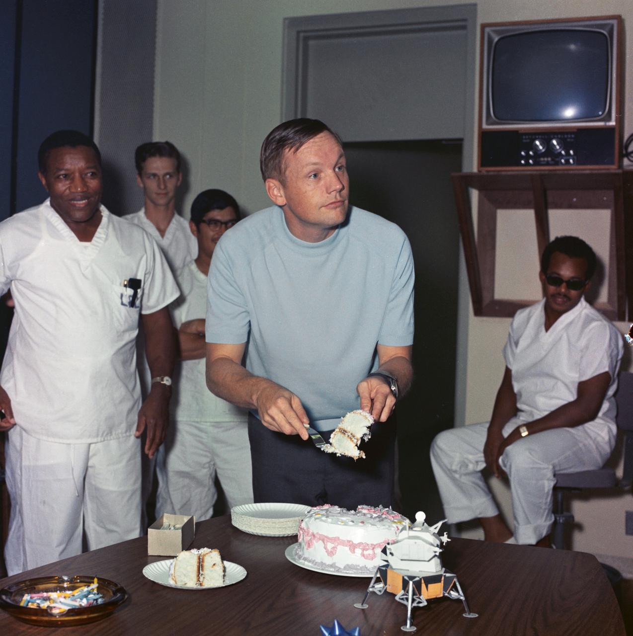 S69-40958 (5 August  1969) --- Astronaut Neil A. Armstrong, commander of the historic Apollo 11 lunar landing mission, and the first man to set foot on the Moon, cuts his birthday cake as he celebrated his 39th birthday.  The crew still confined to the Crew Reception Area (CRA) of the Manned Spacecraft Center's (MSC) Lunar Receiving Laboratory (LRL).  Armstrong was born on August 5, 1930, in Wapakoneta, Ohio.  The cake was described as "standard two-layer, plain vanilla" on which was placed 39 candles.  Eighteen of the persons quarantined with Armstrong assembled and sang happy birthday; and a champagne toast was offered.  CRA support personnel are in the background.  Astronauts Armstrong; Michael Collins, command module pilot; and Edwin E. Aldrin Jr., lunar module pilot, will be released from quarantine on August 11, 1969.