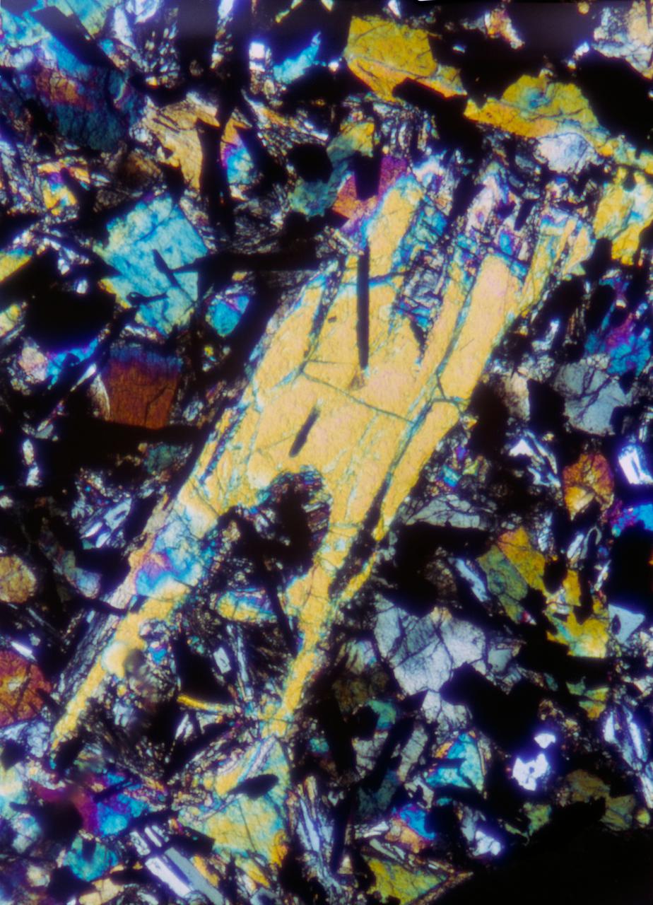 S69-47900 (September 1969) --- This is a photo micrograph of lunar sample 10022. Magnification one inch equals one-tenth millimeter. The light blue and white mineral is plagioclase. The black is ilmenite, and the blue and/or green and/or orange and/or yellow and/or red mineral is pyroxene. The large pyroxene is a phenocryst that had been partially resorbed. The lunar samples collected by astronauts Neil A. Armstrong and Edwin E. Aldrin Jr. during the Apollo 11 lunar landing mission have been subjected to extensive tests and examinations at the Manned Spacecraft Center’s Lunar Receiving Laboratory.