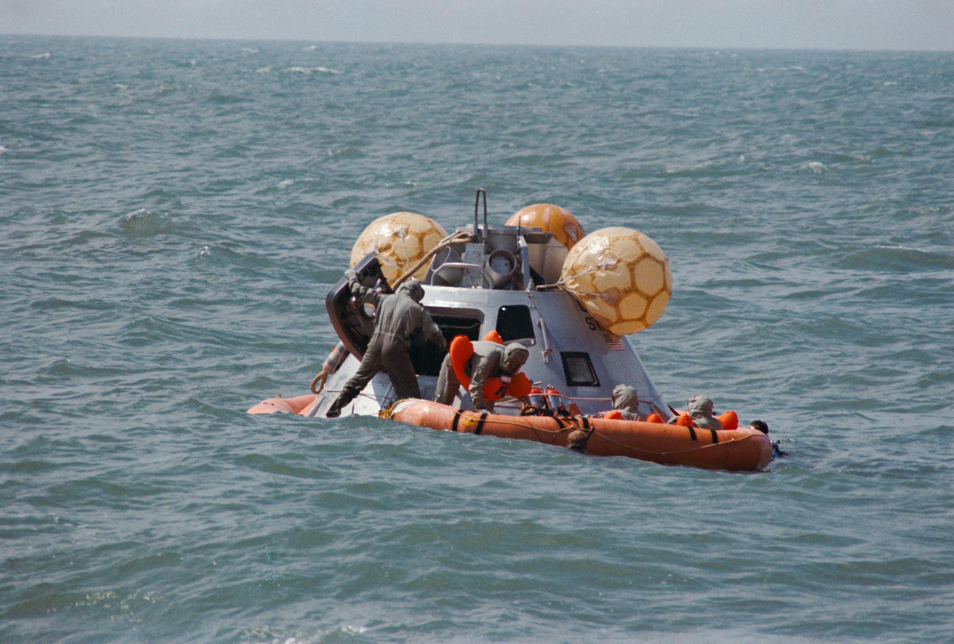 A command module trainer floats on the water as the Apollo 12 crew climbs into a raft during egress training