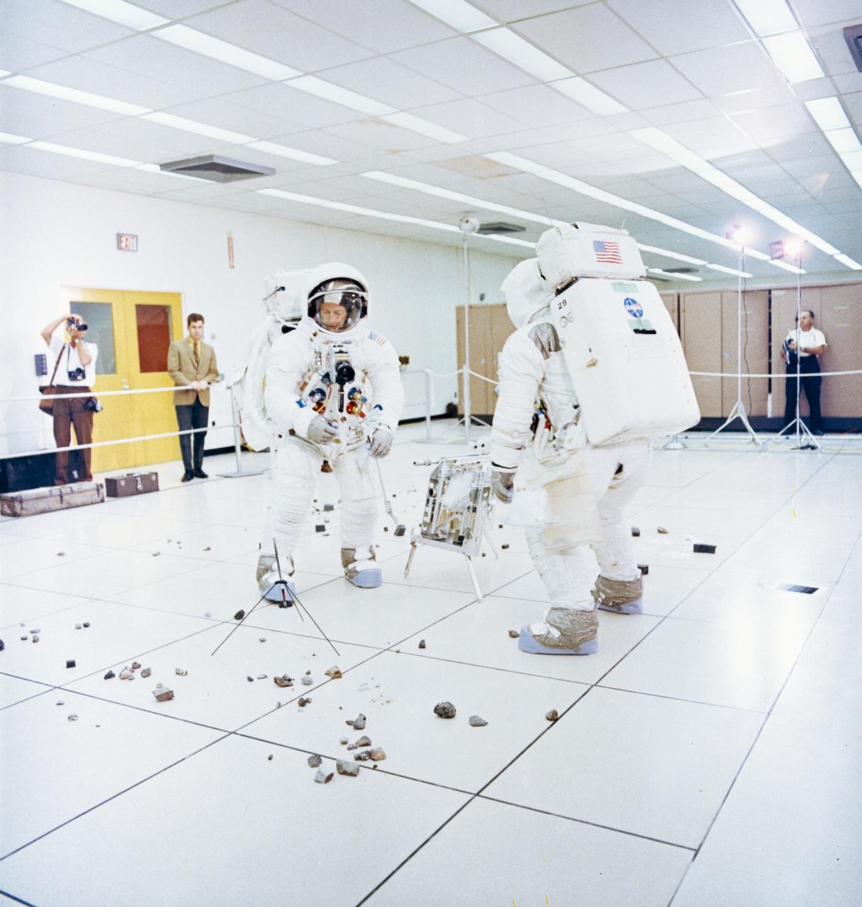 S69-55368 (6 Oct. 1969) --- Two members of the Apollo 12 lunar landing mission participate in lunar surface extravehicular activity (EVA) simulations in the Flight Crew Training Building at the Kennedy Space Center (KSC). Astronaut Charles Conrad Jr., commander (facing camera), simulates picking up samples. Astronaut Alan L. Bean, lunar module pilot, simulates photographic lunar rock sample documentation.
