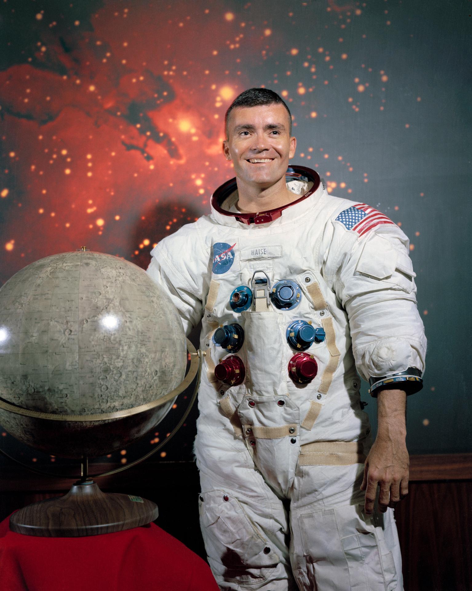 Astronaut Fred Haise poses for his official NASA portrait with a globe of the moon and a starry background behind him.