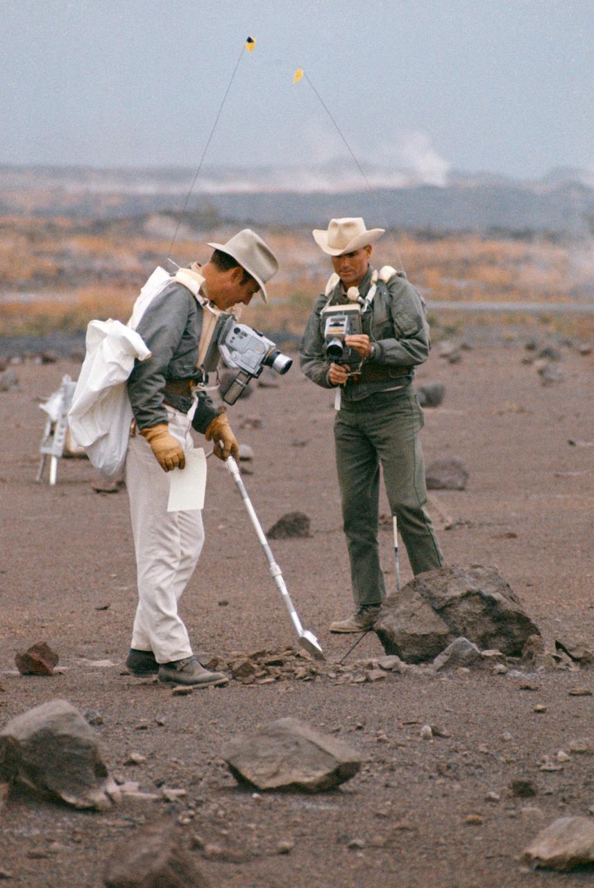 S70-20253 (December 1969) --- Astronauts James A. Lovell Jr. (left) commander, and Fred W. Haise Jr., lunar module pilot, carry out a simulation of a lunar traverse at Kilauea, Hawaii, site. Both crew members of NASA's third team of moon explorers were carrying cameras and communications equipment during the simulated traverse. They maintained contact with men in the roles of spacecraft throughout the traverse. Lovell holds a scoop for the Apollo Lunar Hand Tools (ALHT) and a gnomon, also for the ALHT is deployed in front of Haise. The ALHT carrier is at left background, (almost obscured by Lovell).