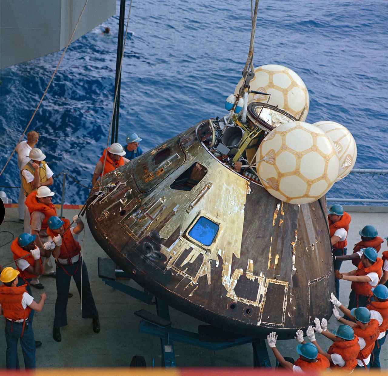 S70-35632 (17 April 1970) --- Crewmen aboard the USS Iwo Jima, prime recovery ship for the Apollo 13 mission, guide the Command Module (CM) atop a dolly onboard the ship. The CM is connected by strong cable to a hoist on the vessel. The Apollo 13 crewmembers, astronauts James A. Lovell Jr., commander; John L. Swigert Jr., command module pilot; and Fred W. Haise Jr., lunar module pilot, were already aboard the USS Iwo Jima when this photograph was made. The CM, with the three tired crewmen aboard, splashed down at 12:07:44 p.m. (CST), April 17, 1970, only about four miles from the recovery vessel in the South Pacific Ocean.