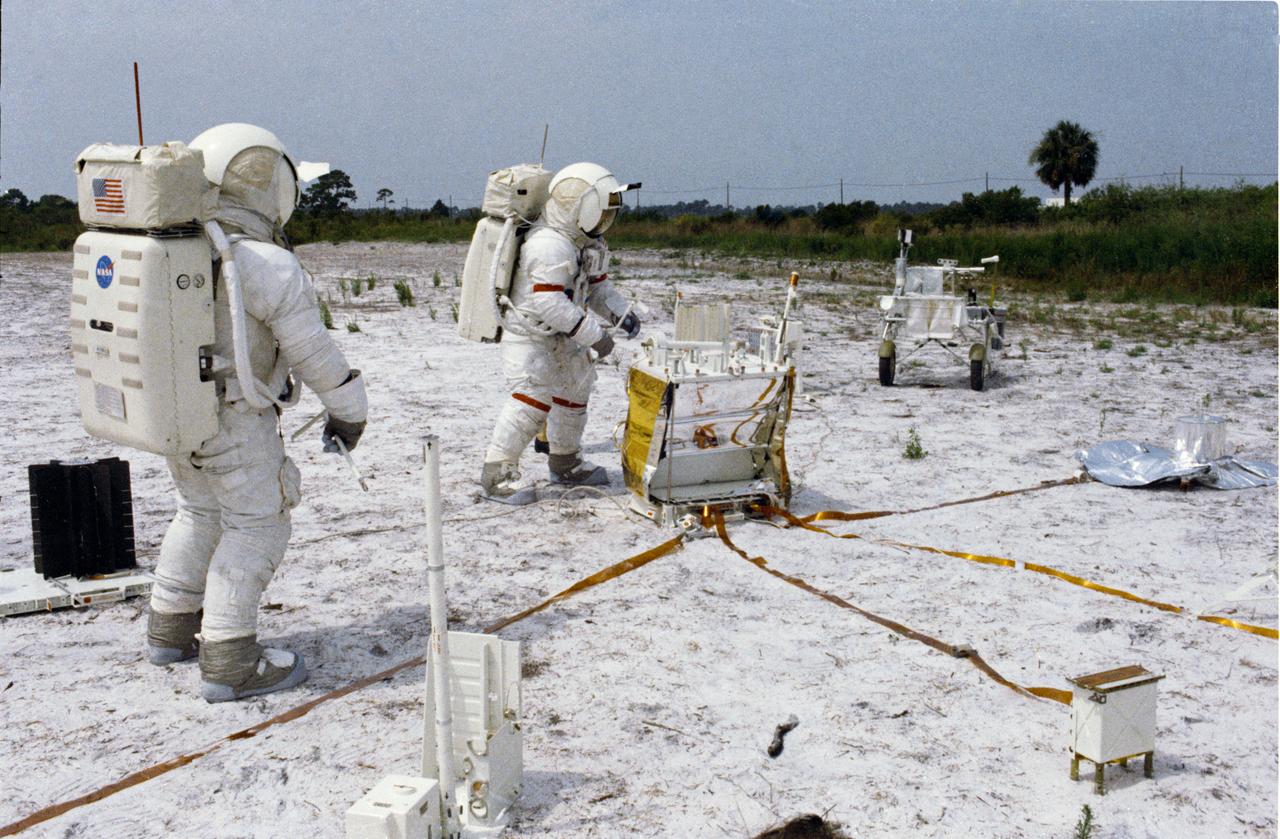 S70-46152 (July 1970) --- Two crew men of the Apollo 14 lunar landing mission participate in lunar surface simulation training at the Kennedy Space Center (KSC). They are deploying components of the Apollo lunar surface experiments package (ALSEP). Standing in the center next to the ALSEP central station is astronaut Alan B. Shepard Jr. (wearing red stripe on space suit), commander. Astronaut Edgar D. Mitchell, lunar module pilot, is in the left foreground. Both crew men are wearing the Extravehicular Mobility Units (EMU).