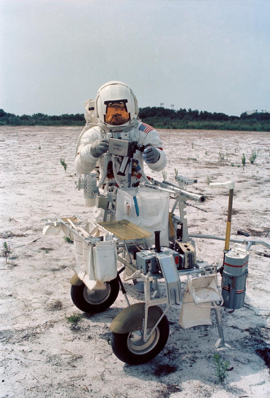 S70-46191 (July 1970) --- Astronaut Alan B. Shepard Jr., commander of the Apollo 14 lunar landing mission, participates in lunar surface training at the Kennedy Space Center (KSC). Shepard is adjusting a camera mounted to the modular equipment transporter (MET). The MET, nicknamed the "Rickshaw", will serve as a portable work bench with a place for the Apollo lunar hand tools and their carrier, three cameras, two sample container bags, a special environment sample container, spare magazines, and a lunar surface Penetrometer. Shepard is wearing an Extravehicular Mobility Unit (EMU).