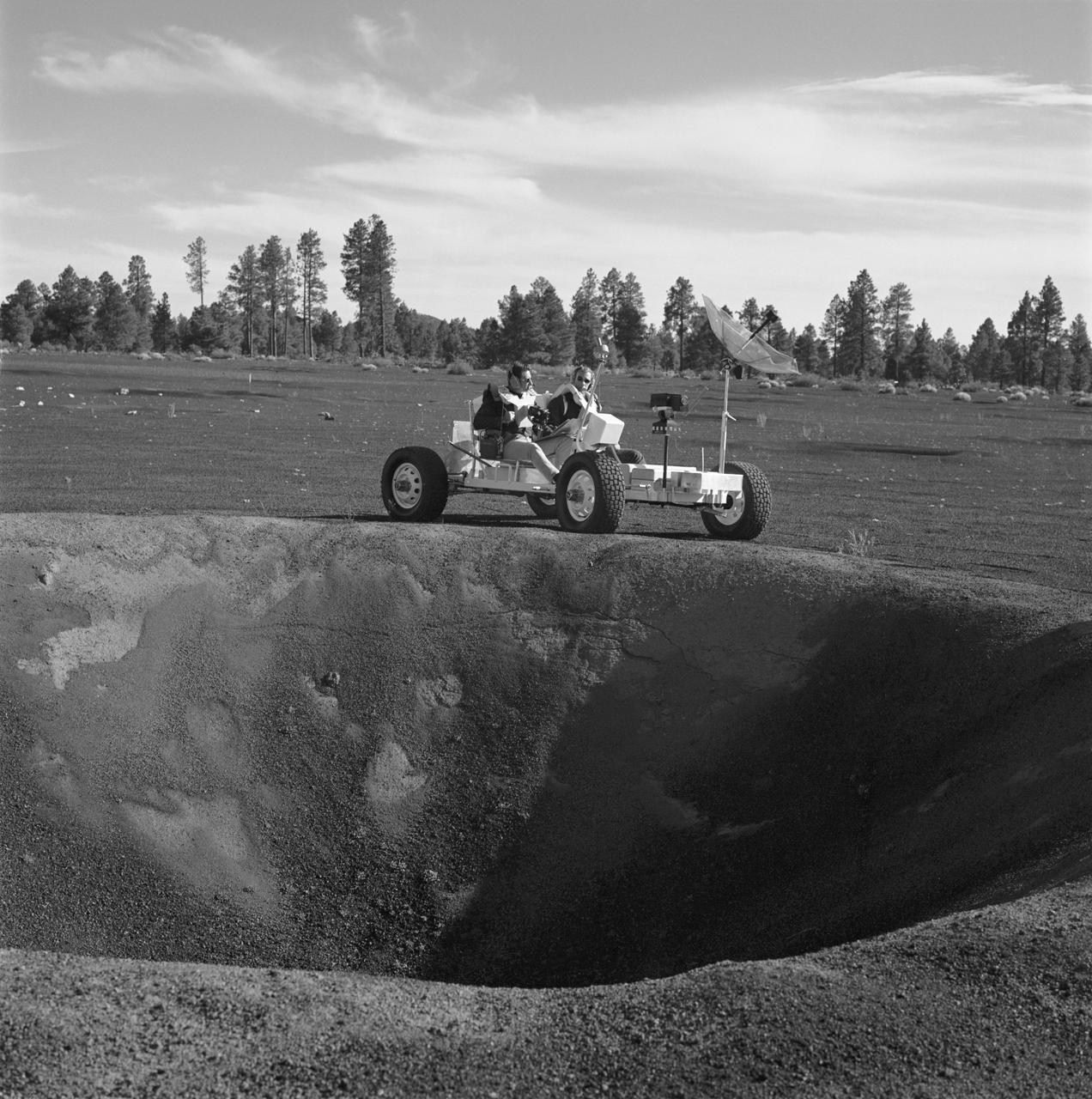 S70-53300 (2-3 Nov. 1970) --- Two Apollo 15 crew members, riding a Lunar Roving Vehicle (LRV) simulator, participate in geology training at the Cinder Lake crater field in Arizona. Astronaut David R. Scott, Apollo 15 commander, seated on the left; and to Scott's right is astronaut James B. Irwin, lunar module pilot. They have stopped at the rim of a 30-feet deep crater to look over the terrain. The simulator, called "Grover", was built by the United States Geological Survey.